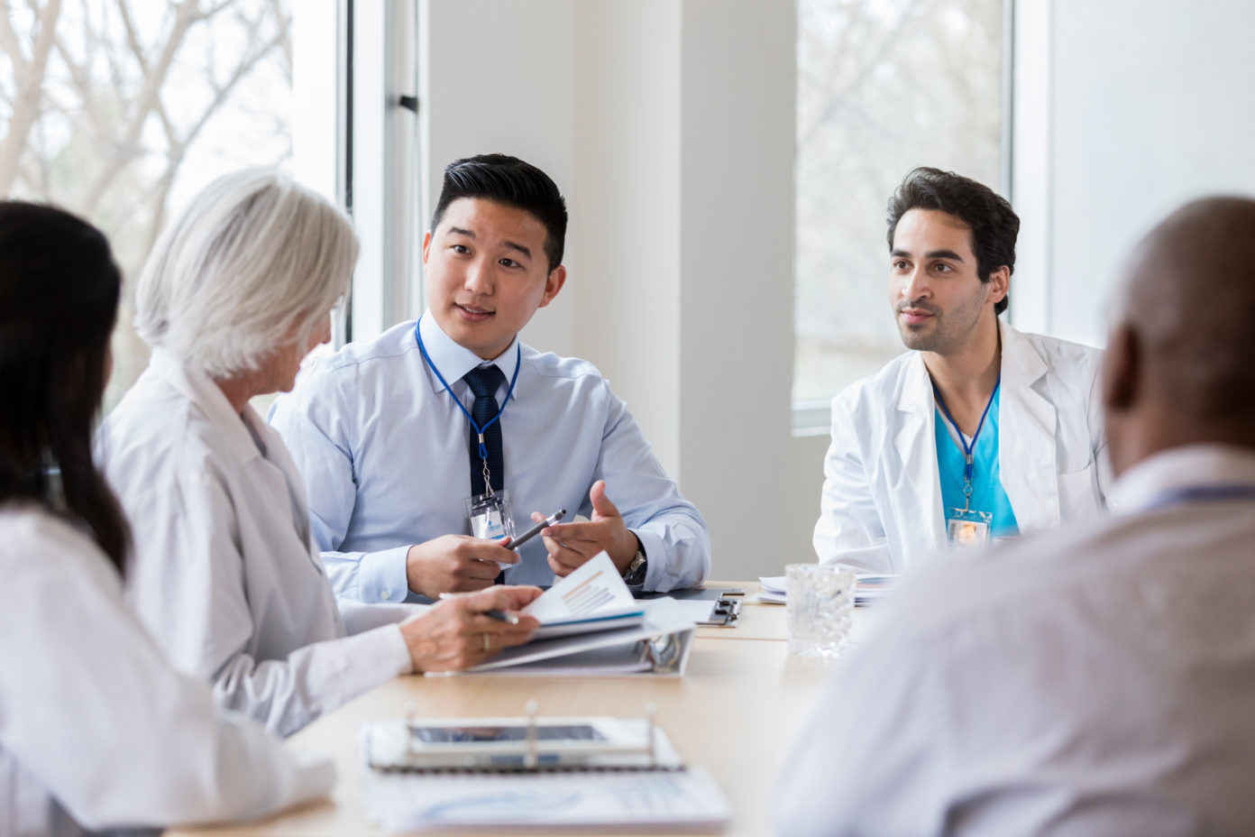 Mid adult male hospital administrator gestures while discussing hospital business with a female doctor during a staff meeting.